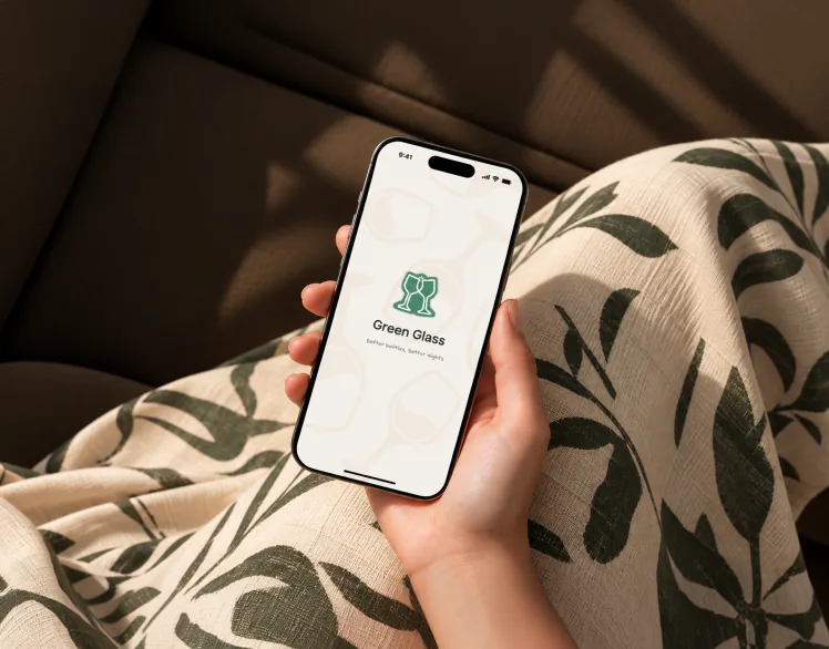 A hand holding a phone open on the Green Glass splash screen, on a leaf-print throw